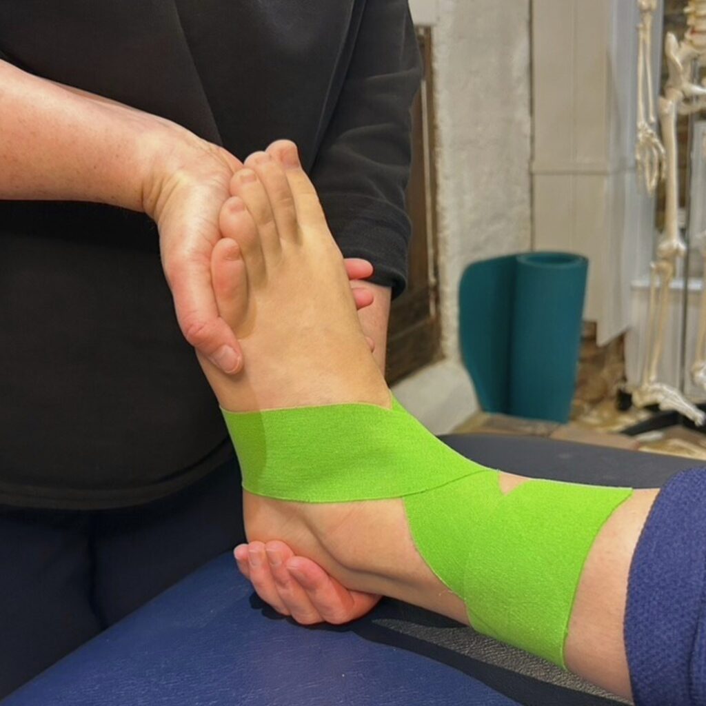 Patient wearing green sports tape on ankle while physiotherapist provides support.