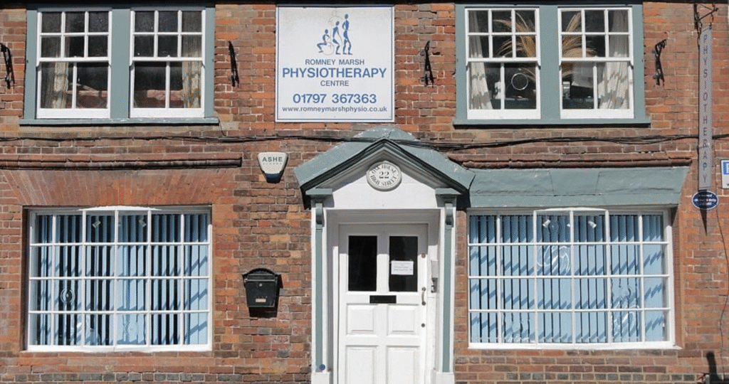 Quaint orange brick building with warm blue door frame and windows, featuring clinic branding on Romney Marsh High Street.